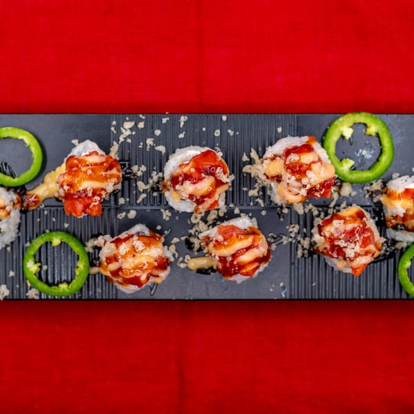 Tanpopo Ramen & Sushi Restaurant's sushi rolls with sauce and green pepper slices on a black tray.