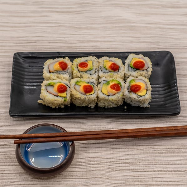 Eight sushi rolls with avocado, crab, and spicy sauce on a black plate with chopsticks.