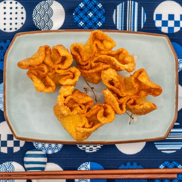 Crispy golden crab rangoons on a light blue rectangular plate, set on a blue and white patterned cloth.