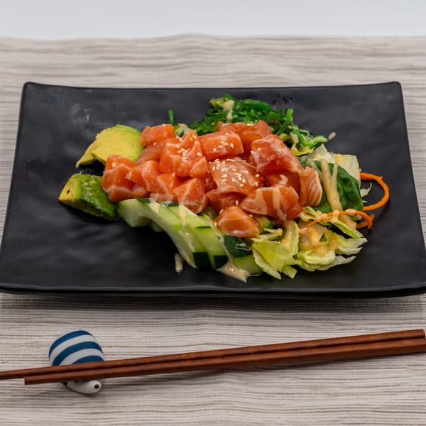 Tanpopo Ramen & Sushi Restaurant's salmon poke salad with avocado, cucumber, and seaweed on a black plate.