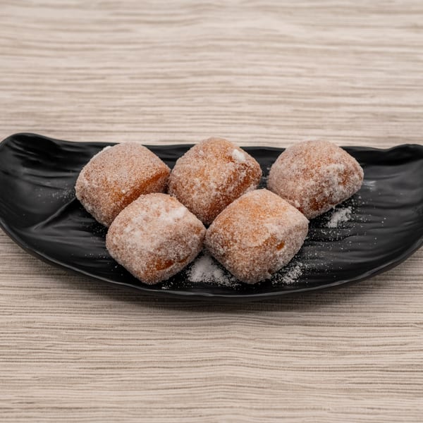 Five sugar-dusted Japanese donuts, known as beignets, arranged on a black plate.