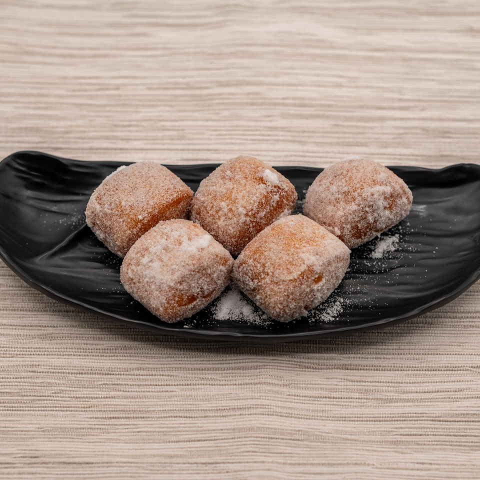 Five sugar-dusted Japanese donuts, known as beignets, arranged on a black plate.