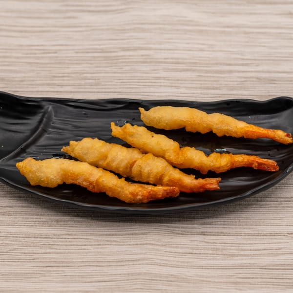 Five golden-brown tempura shrimp, with visible tails, arranged on a black, fish-shaped plate.
