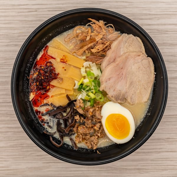 Overhead view of Tanpopo Ramen with pork, egg, bamboo shoots, and chili oil in a black bowl.